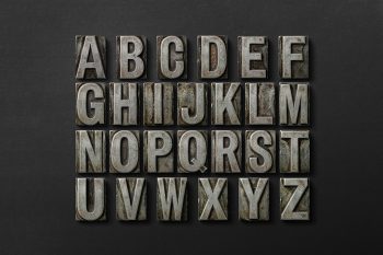 Metal letterpress alphabet grid with 26 uppercase letters arranged on dark background for typography and print design.