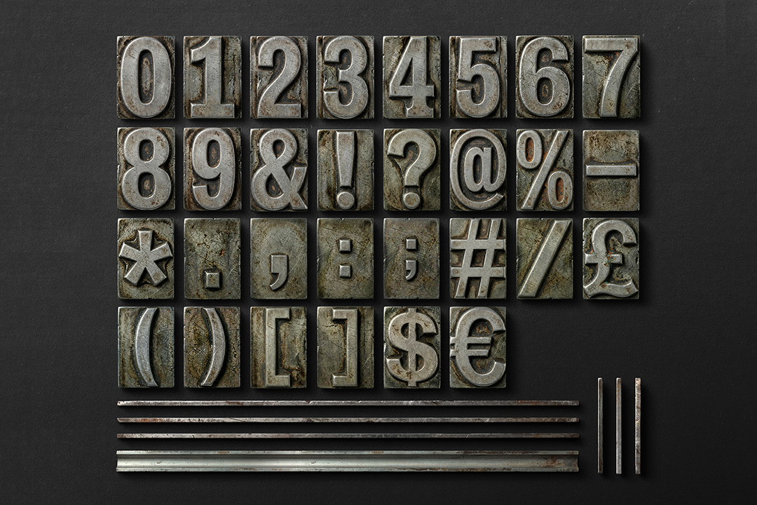 Metal letterpress numbers and symbols set with dividers arranged on dark surface for editorial and typography compositions.