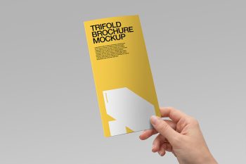 A hand holding a trifold brochure mockup with yellow front cover and bold black typography on a light grey background.
