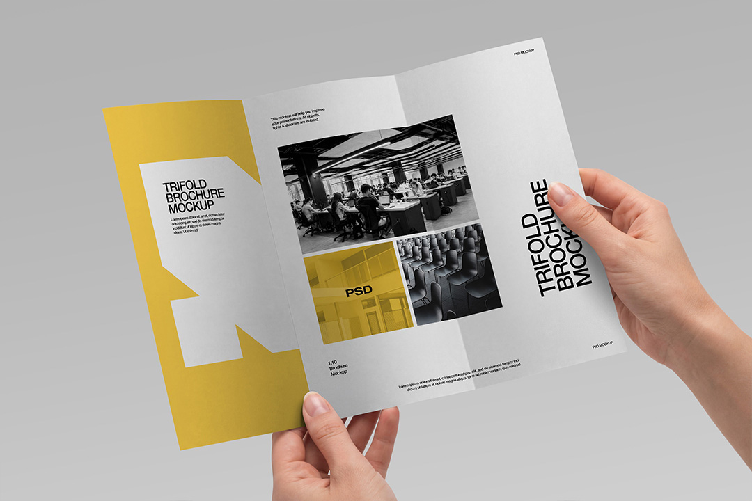 Two hands holding an open trifold brochure mockup displaying interior panels with yellow accents and editorial layout on grey.