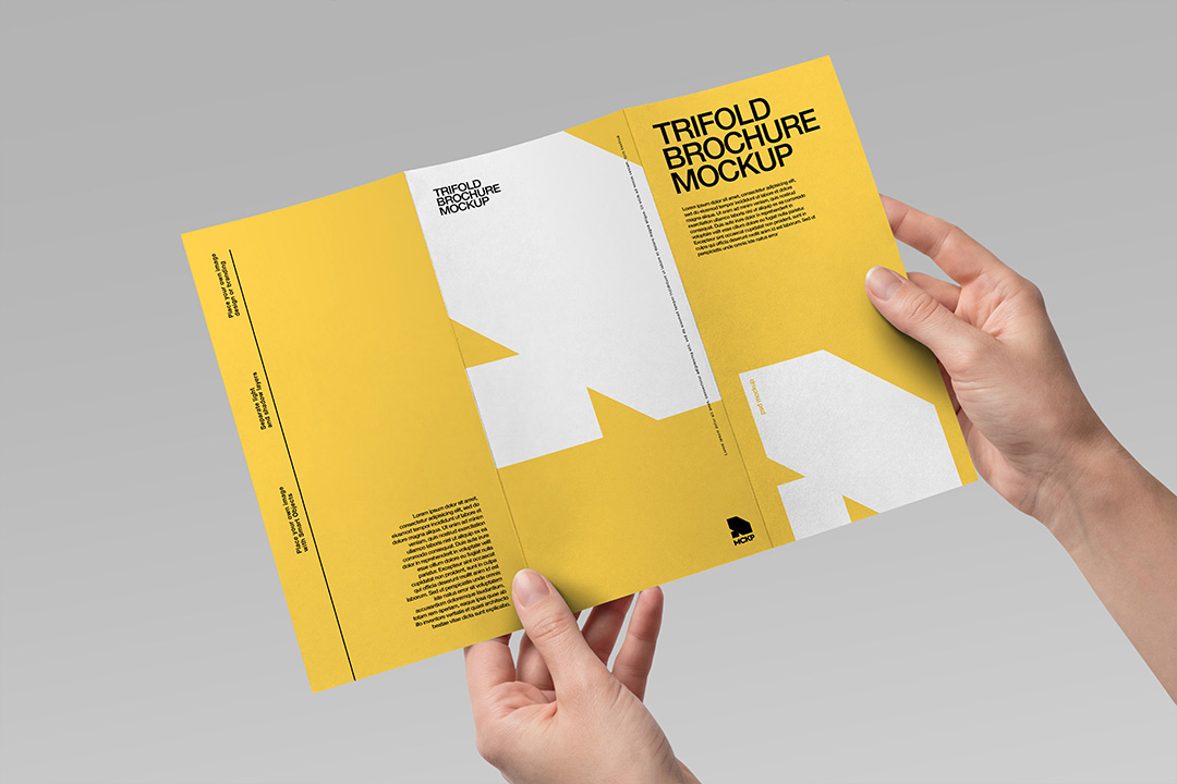 Two hands holding an open trifold brochure mockup displaying the full unfolded yellow and white inner spread on a grey background.