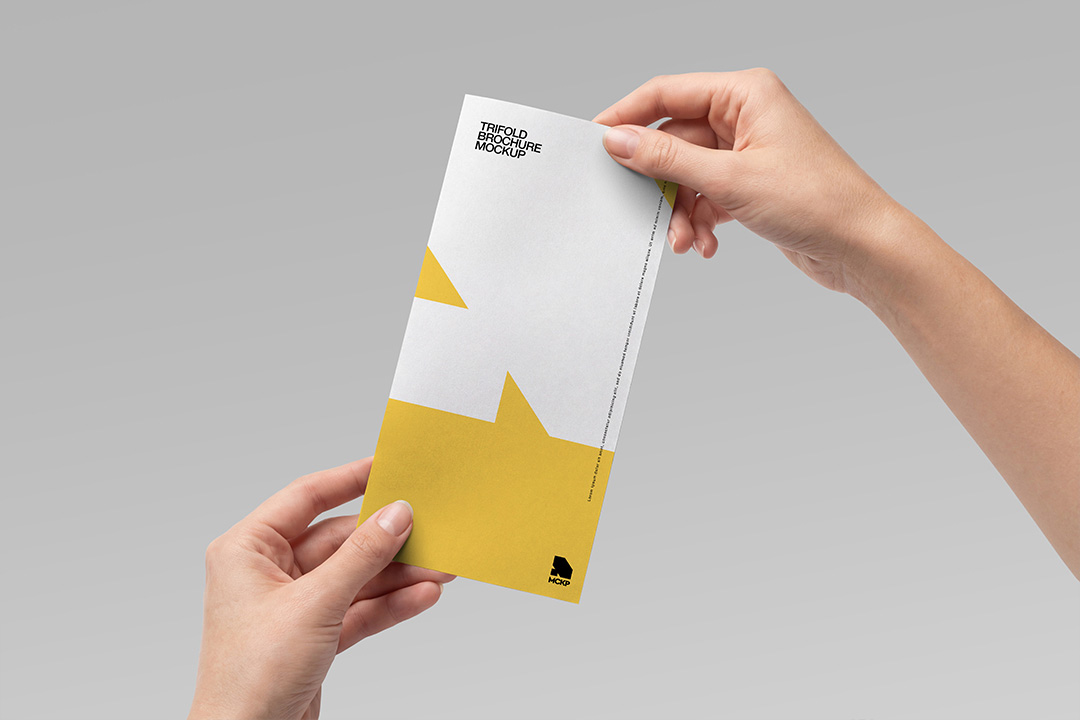 Two hands holding a closed trifold brochure mockup showing the back cover with yellow and white geometric design on grey background.