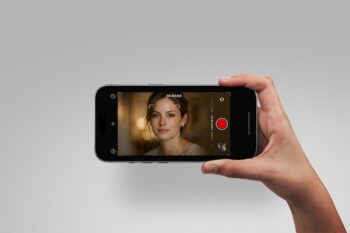 Hand holding iPhone video mockup sideways on grey background, screen showing a camera recording interface with red button