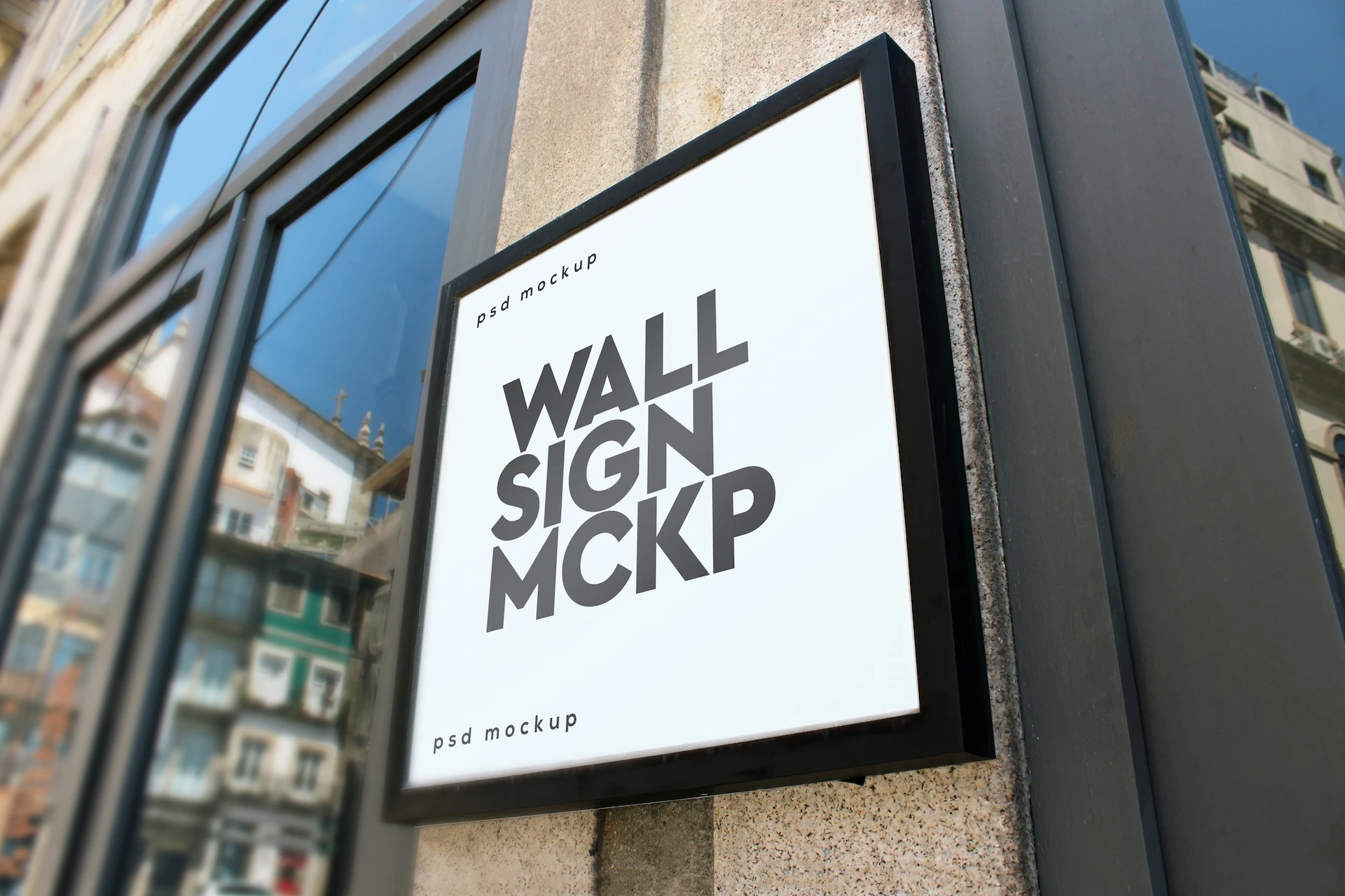 Wall sign mockup set framed white sign on a stone column beside glass windows reflecting the buildings across the street